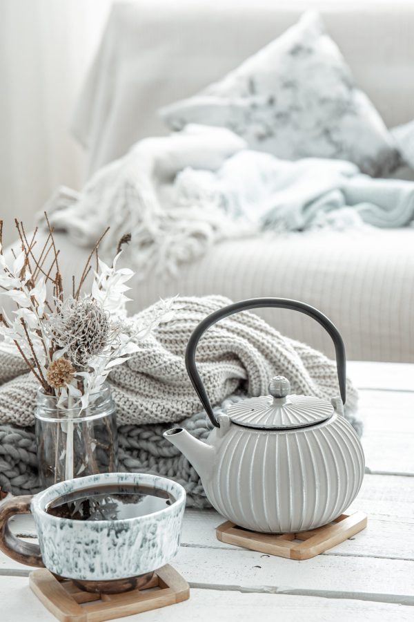 A teapot and a beautiful ceramic cup with decor details in a hygge style living room. The concept of home comfort and modern style.